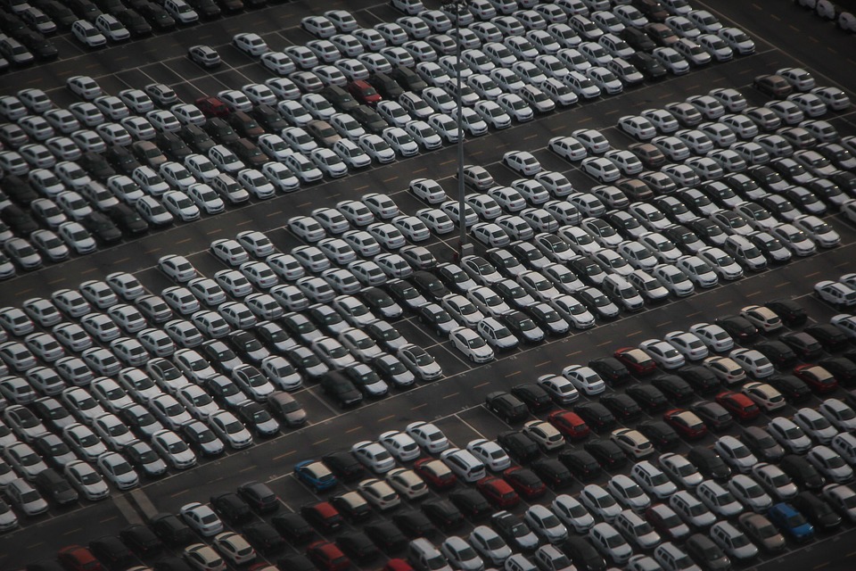 picture overhead of hundreds of cars in a parking lot, a mix of white, gray, red, and brown cars