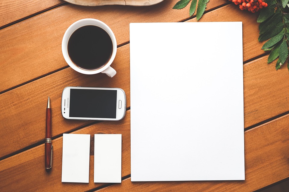 picture of a piece of paper, a pen, a phone, a cup of coffee, and a notepad